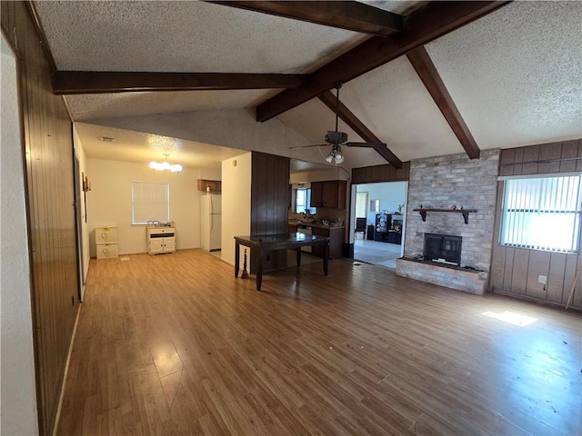 unfurnished living room featuring vaulted ceiling with beams, ceiling fan with notable chandelier, a fireplace, wood finished floors, and a textured ceiling