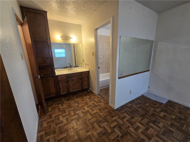 bathroom featuring baseboards, a bathing tub, a textured ceiling, and vanity