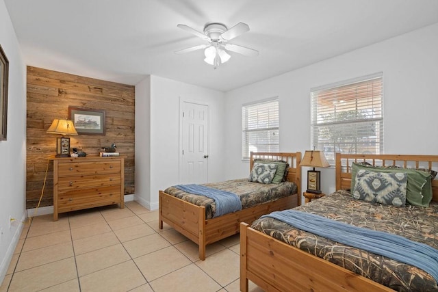 bedroom with light tile patterned floors, an accent wall, wood walls, a ceiling fan, and baseboards