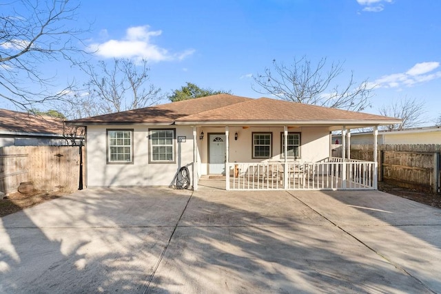 ranch-style home with a shingled roof, covered porch, fence, and stucco siding