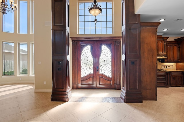 foyer entrance with french doors, light tile patterned floors, crown molding, and a notable chandelier