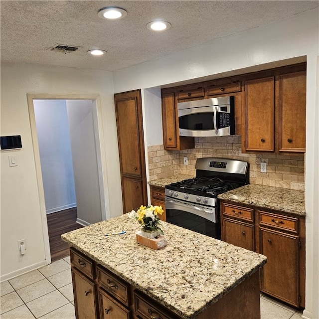 kitchen featuring light tile patterned flooring, light stone countertops, a textured ceiling, and appliances with stainless steel finishes