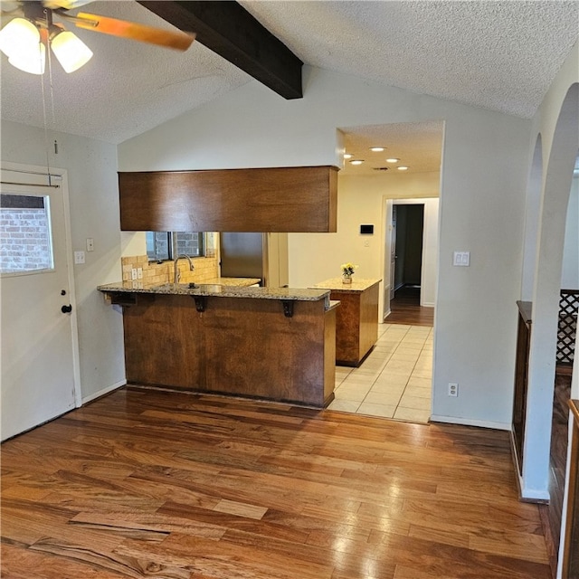 kitchen with a textured ceiling, vaulted ceiling with beams, light hardwood / wood-style flooring, and kitchen peninsula