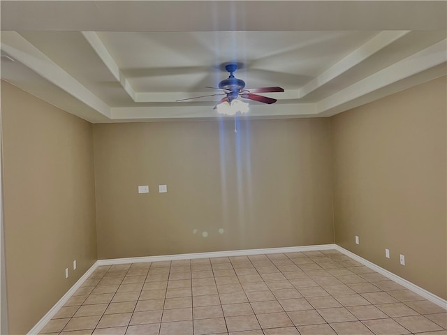 tiled empty room featuring ceiling fan and a raised ceiling