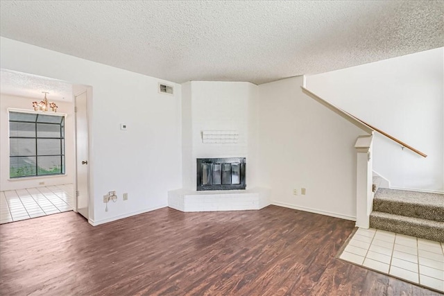 6702 Everhart Unit N102, Corpus Christi, TX 78413 - unfurnished living room with a textured ceiling, wood finished floors, stairway, a brick fireplace, and a chandelier