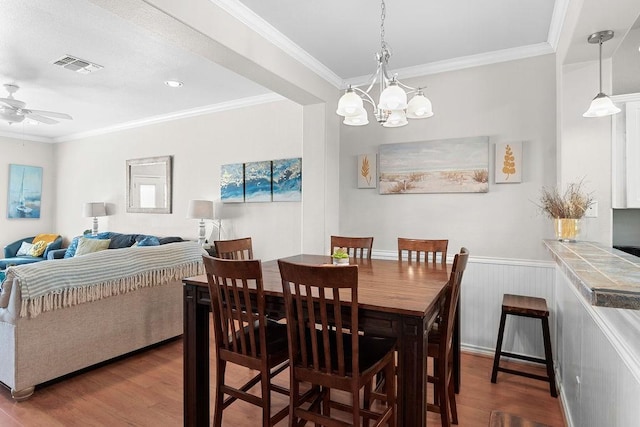 dining area featuring ceiling fan with notable chandelier, visible vents, crown molding, and wood finished floors