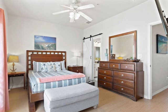 bedroom with light wood finished floors, a barn door, visible vents, and baseboards