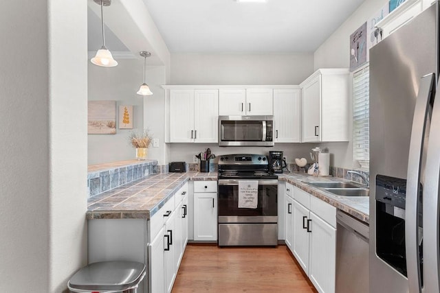 kitchen with white cabinets, light wood finished floors, stainless steel appliances, and a sink