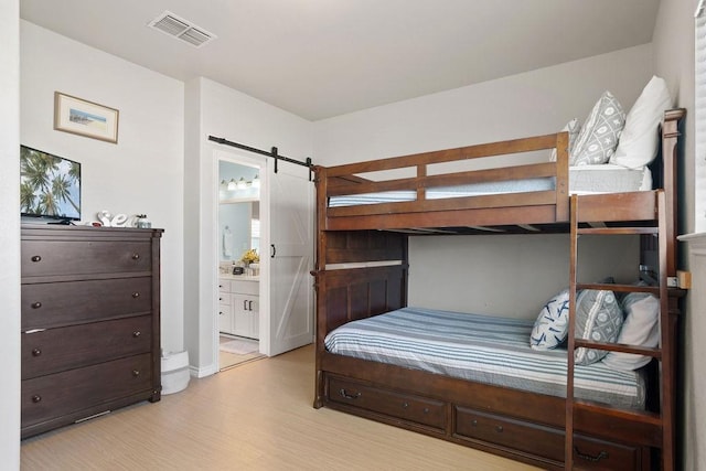 bedroom with visible vents, light wood-style flooring, ensuite bathroom, and a barn door