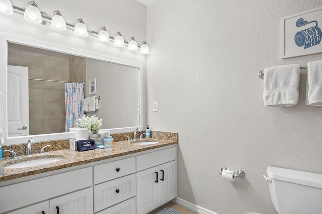 bathroom with toilet, double vanity, a tile shower, and a sink