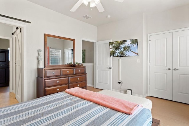 bedroom with light wood finished floors, a closet, visible vents, a barn door, and a ceiling fan