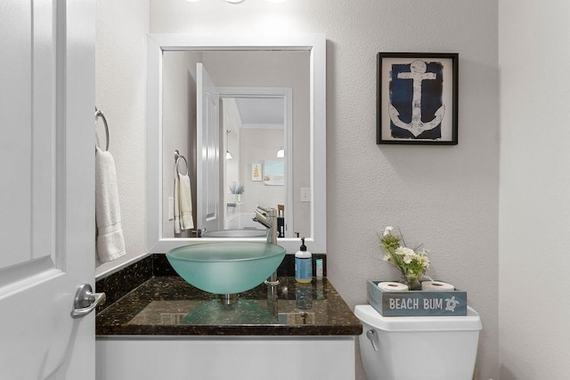 half bath with toilet, a textured wall, ornamental molding, and vanity