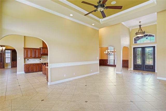 entrance foyer with a high ceiling, a raised ceiling, light tile patterned floors, and ornamental molding