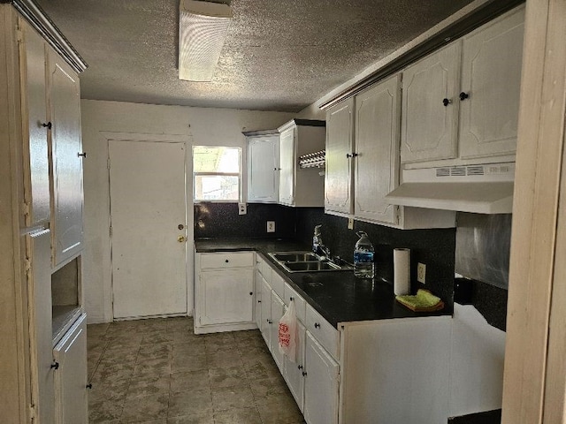 kitchen with a sink, under cabinet range hood, dark countertops, white cabinetry, and decorative backsplash