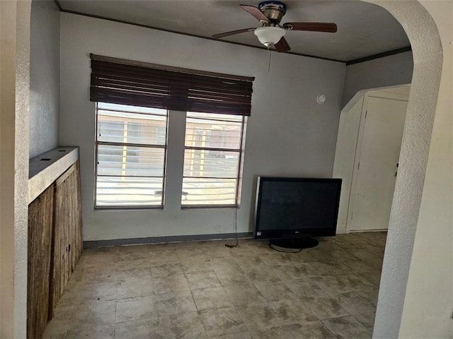 unfurnished living room with arched walkways, a healthy amount of sunlight, baseboards, and a ceiling fan