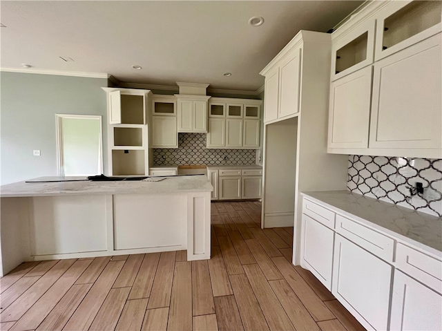 kitchen with backsplash, light stone countertops, ornamental molding, and light hardwood / wood-style flooring