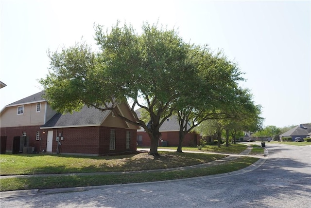 view of side of property featuring central AC unit, brick siding, and a yard