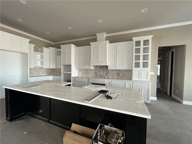 kitchen with a large island, tasteful backsplash, white cabinets, ornamental molding, and light stone counters