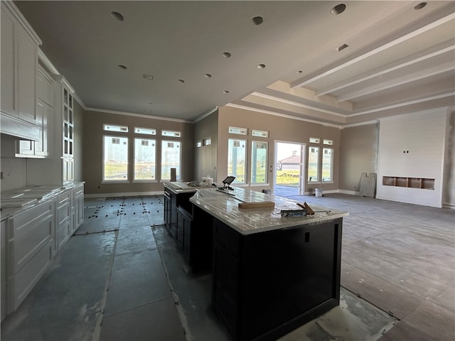 kitchen featuring light stone countertops, white cabinets, a center island, ornamental molding, and a raised ceiling