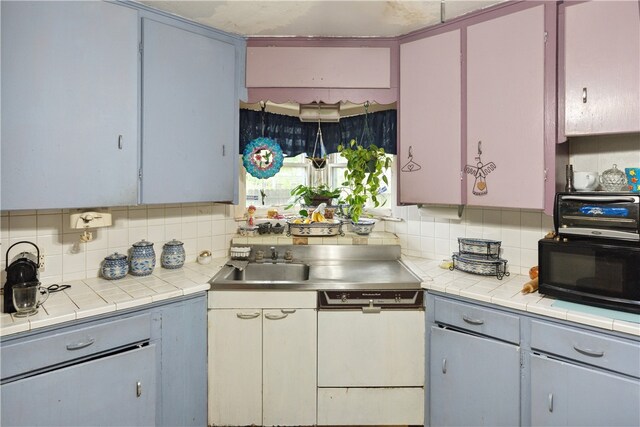 kitchen featuring sink, gray cabinets, white dishwasher, backsplash, and tile counters