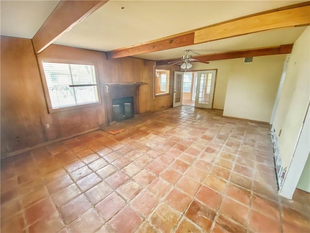 unfurnished living room with beamed ceiling, wood walls, french doors, and a wealth of natural light