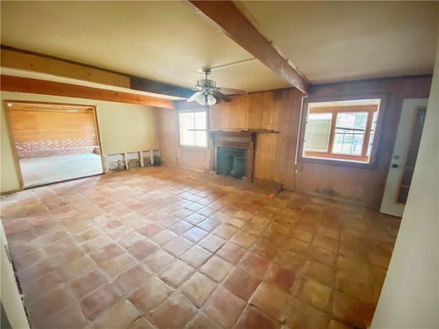 unfurnished living room featuring ceiling fan, wooden walls, beam ceiling, and light tile patterned floors