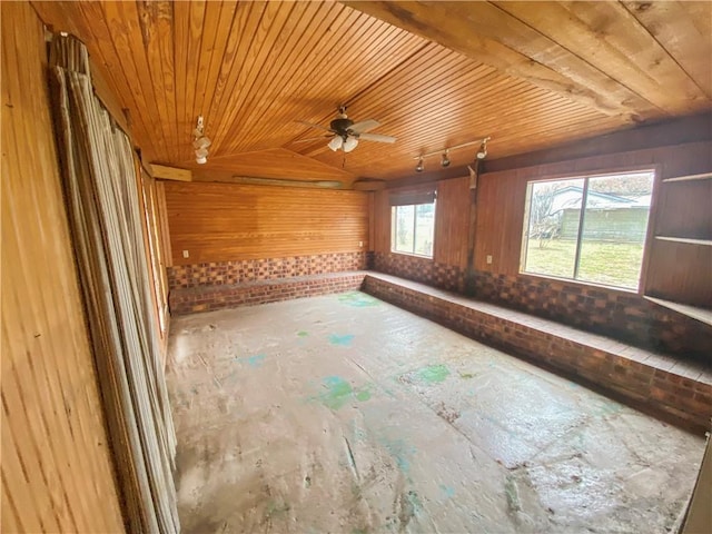 empty room with vaulted ceiling, wooden walls, track lighting, and wood ceiling