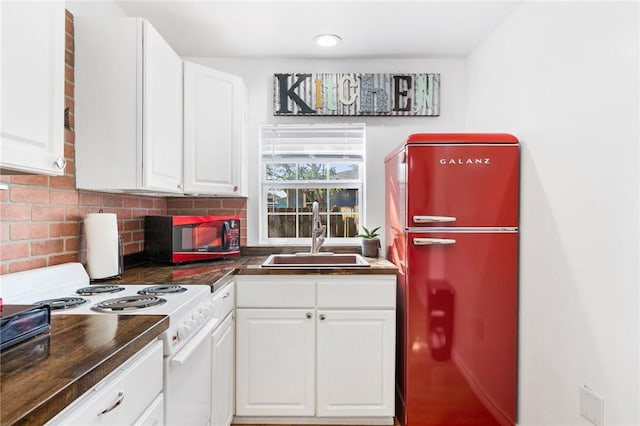 kitchen featuring white range with electric stovetop, dark countertops, refrigerator, white cabinetry, and a sink