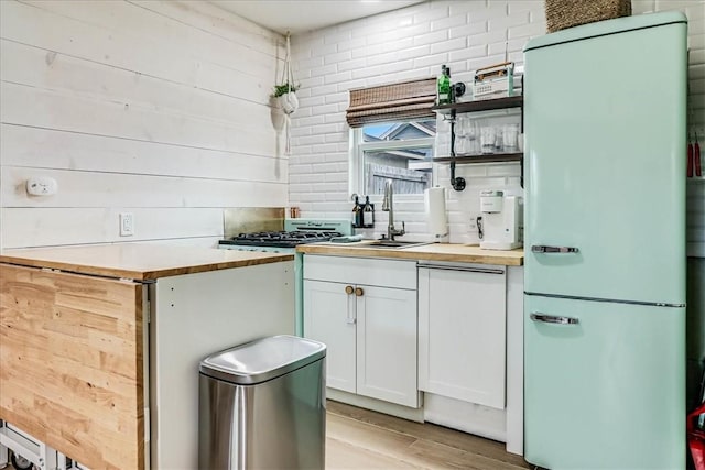 kitchen featuring wooden counters, wooden walls, white cabinets, and refrigerator