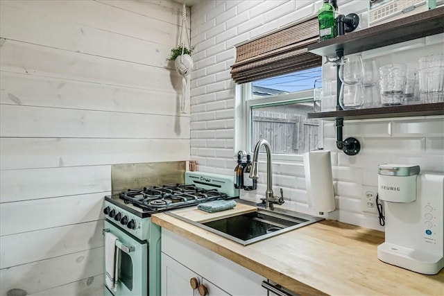 kitchen featuring wooden walls, stainless steel range, sink, and butcher block countertops