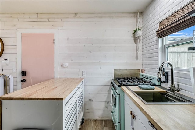 kitchen featuring wooden walls, stainless steel range with gas stovetop, white cabinets, and butcher block countertops