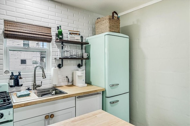 kitchen featuring butcher block counters, sink, white cabinetry, white fridge, and backsplash