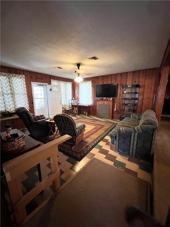 living area with a healthy amount of sunlight, a ceiling fan, visible vents, and wooden walls