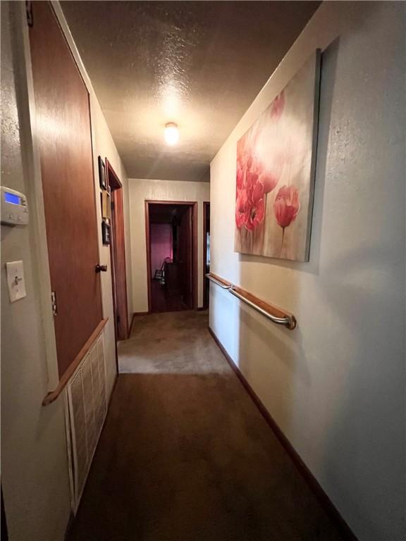 hall with a textured ceiling, carpet floors, and baseboards