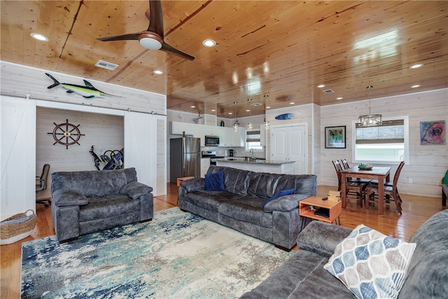 living room with a barn door, light hardwood / wood-style floors, wooden walls, and plenty of natural light