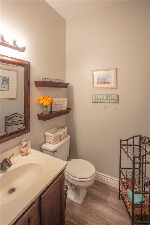 half bathroom featuring baseboards, toilet, wood finished floors, and vanity