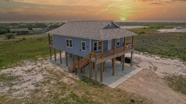13 Bayview Loop, Rockport, TX 78382 - back of house at dusk featuring a carport, driveway, a shingled roof, a patio area, and a wooden deck