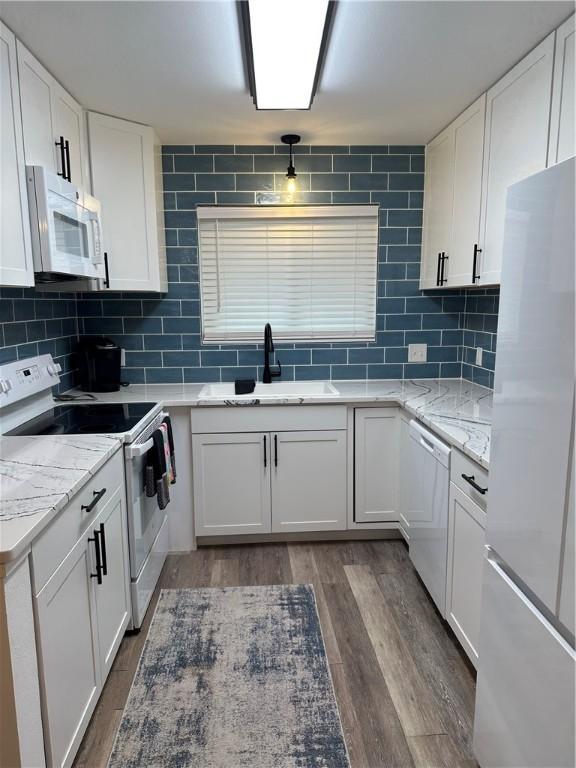 kitchen featuring a sink, backsplash, white cabinets, white appliances, and dark wood-style flooring