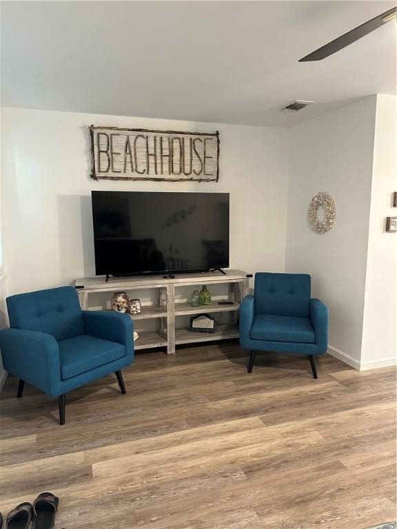 living area featuring visible vents, baseboards, a ceiling fan, and wood finished floors