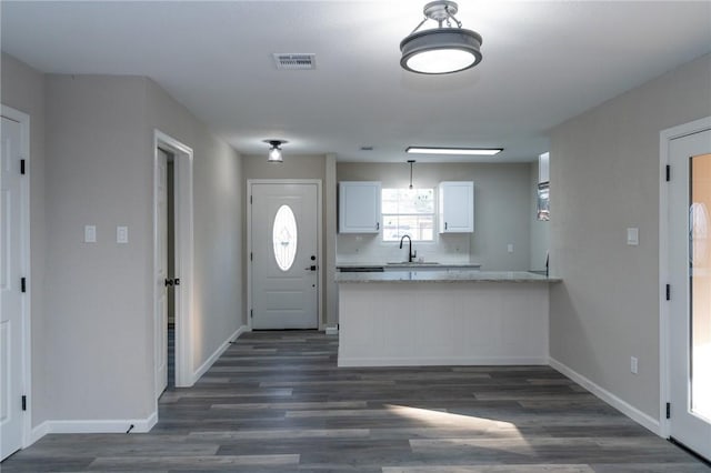 kitchen with light stone countertops, kitchen peninsula, dark hardwood / wood-style flooring, backsplash, and white cabinetry