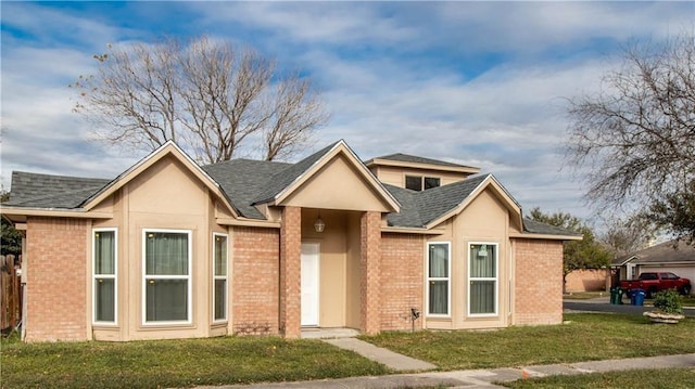 view of front facade with roof with shingles, a front yard, and brick siding