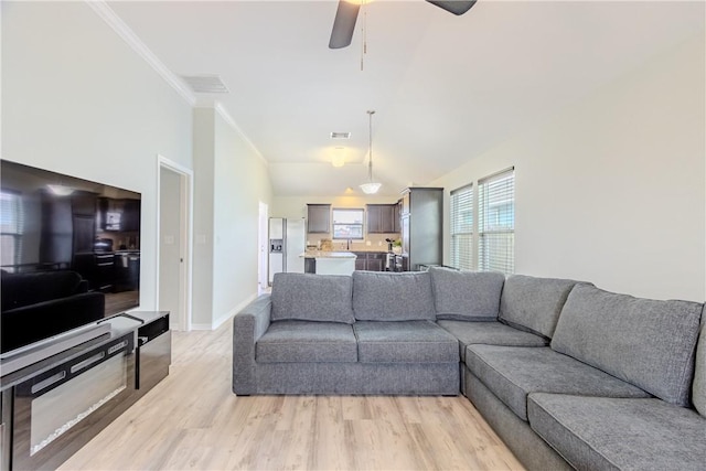 living room featuring light wood-style floors, a ceiling fan, ornamental molding, baseboards, and vaulted ceiling