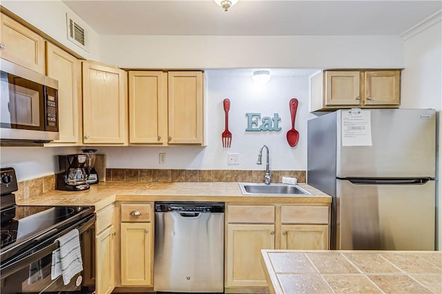 kitchen featuring stainless steel appliances, light brown cabinetry, and a sink