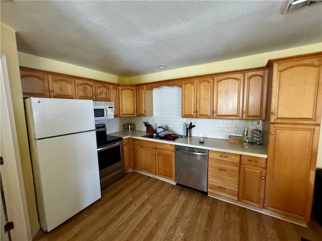 kitchen with backsplash, appliances with stainless steel finishes, a textured ceiling, hardwood / wood-style floors, and sink