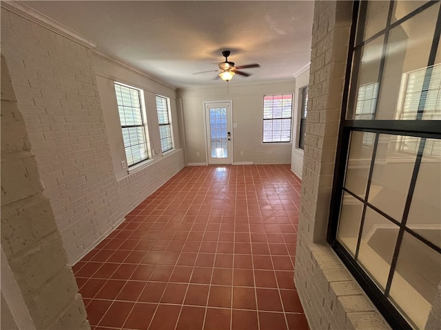 interior space with ceiling fan, a healthy amount of sunlight, brick wall, and ornamental molding