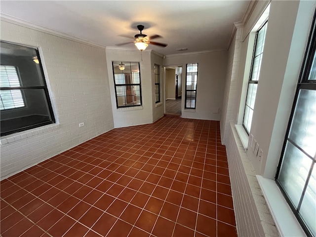 tiled spare room with a wealth of natural light, ceiling fan, brick wall, and ornamental molding