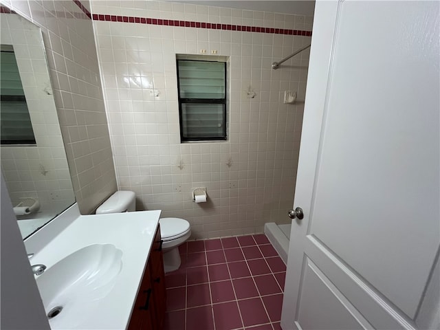 bathroom with a tile shower, tile patterned flooring, toilet, vanity, and tile walls