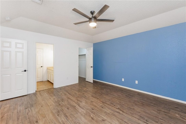 unfurnished bedroom with connected bathroom, a closet, baseboards, a textured ceiling, and wood finished floors