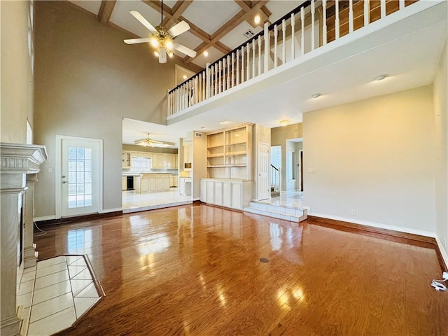 unfurnished living room with coffered ceiling, beamed ceiling, a towering ceiling, hardwood / wood-style flooring, and ceiling fan