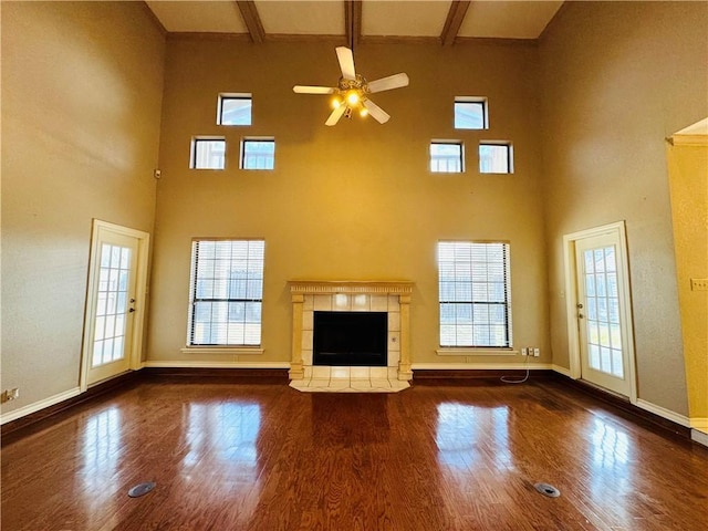 unfurnished living room with a tile fireplace, dark hardwood / wood-style flooring, a high ceiling, ceiling fan, and beam ceiling